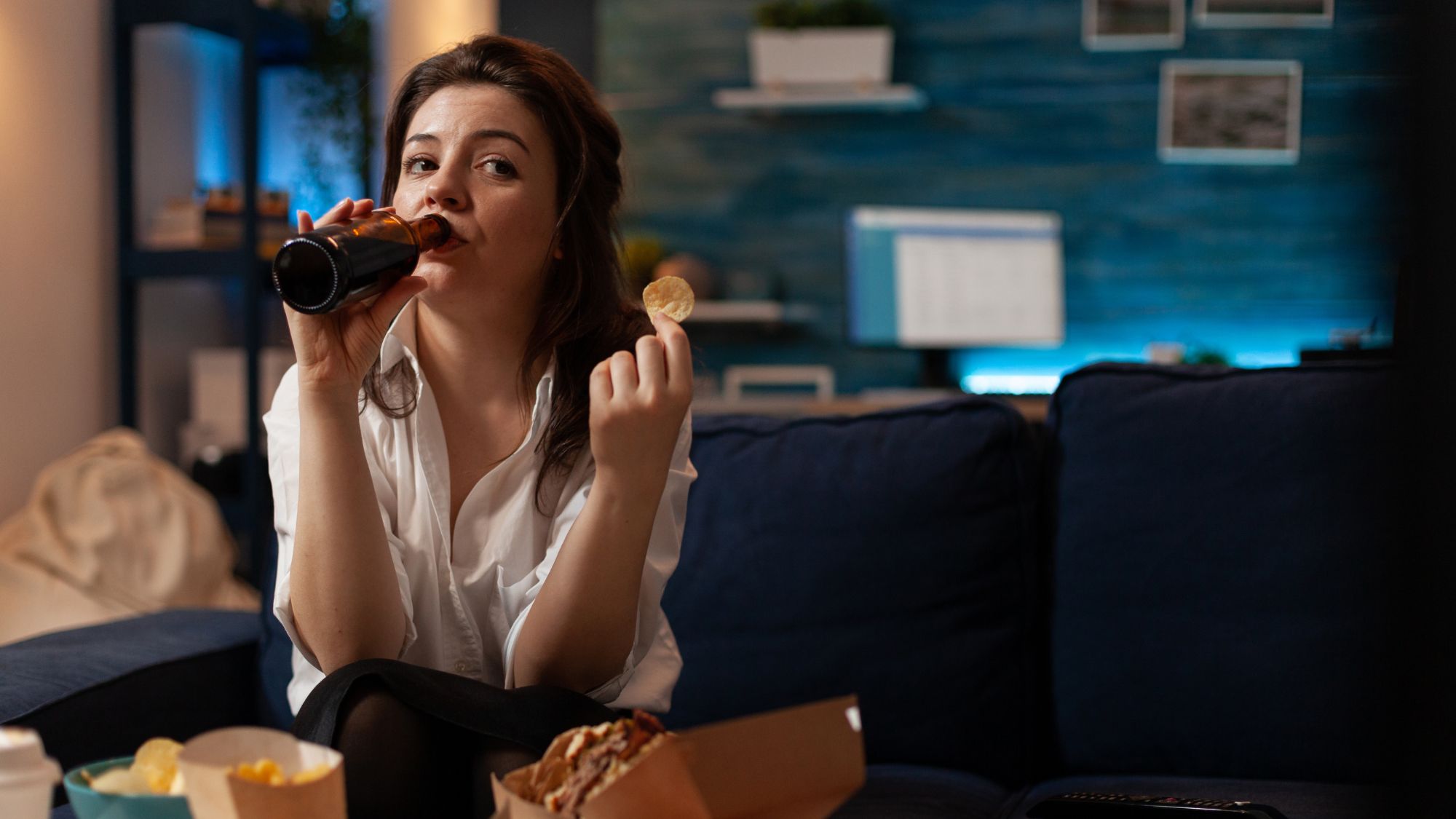 A woman enjoying her leisure time on a couch with a beer and chips, endorsing pizza delivery Stockport.