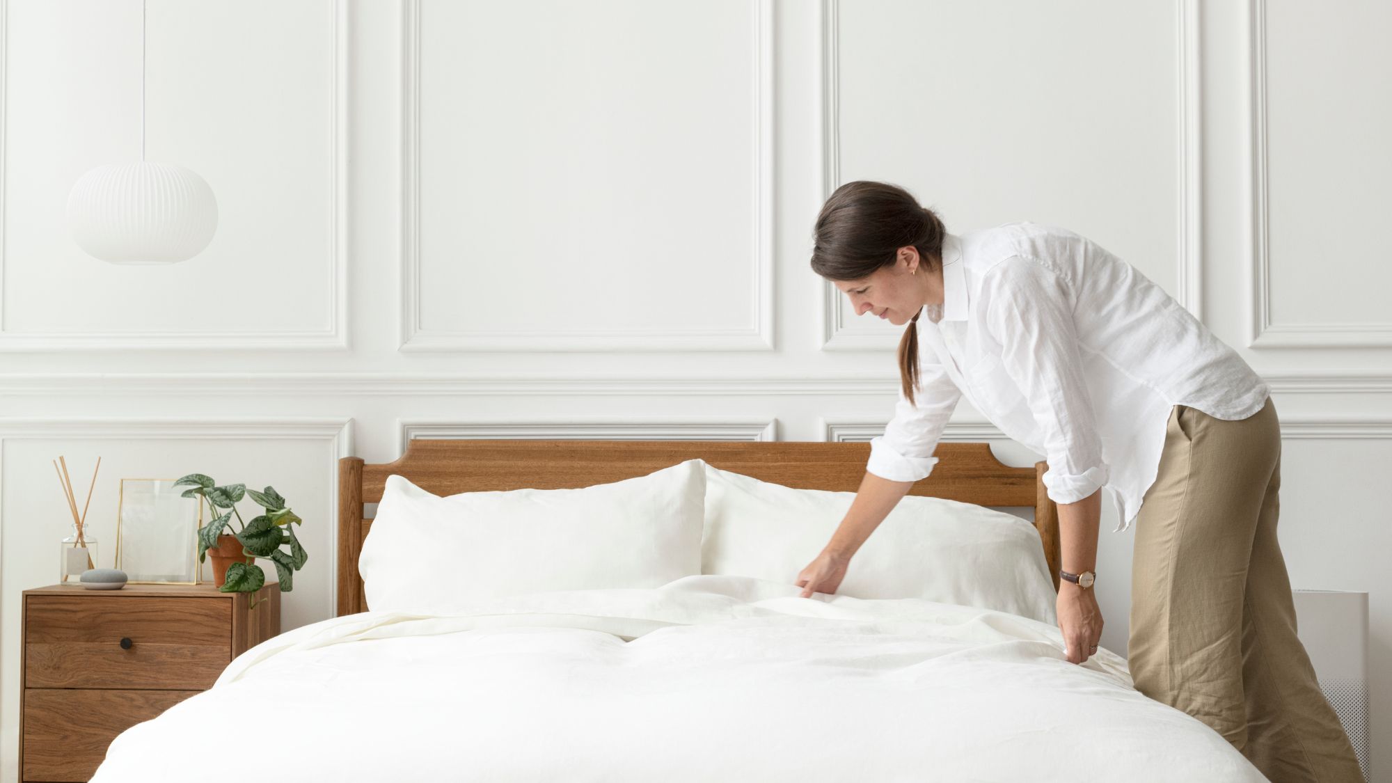 A woman from t & a textiles wholesale bedding suppliers uk is placing a white comforter on a clean bedding.